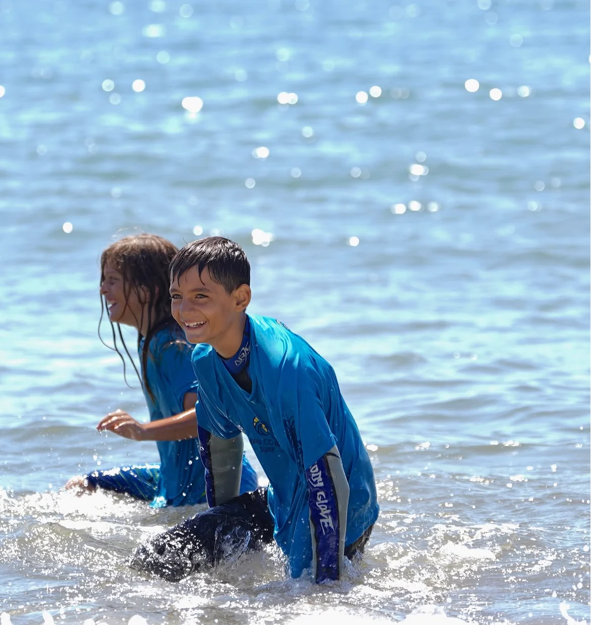 Two young surfers smiling in the sparkling shallows